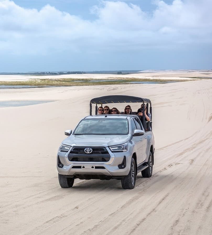 Caminhonete 4x4 aberta atravessando as dunas com um grupo pequeno